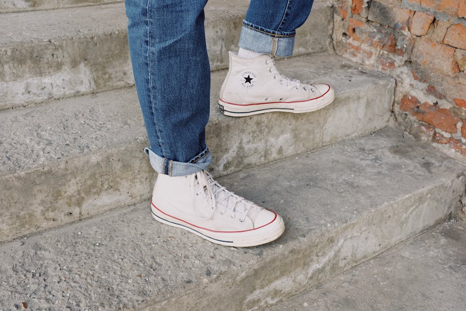 Close-up of white Converse sneakers and jeans on rustic concrete stairs, showcasing urban street style.