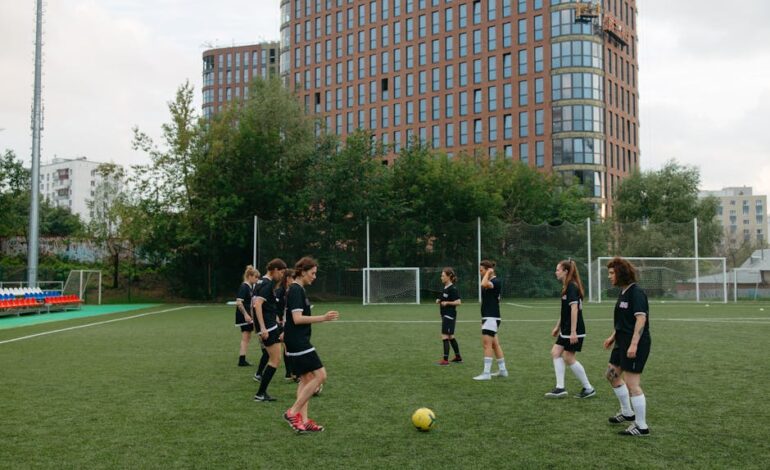 Energetic women's soccer team practicing on a green field with urban buildings in the background.