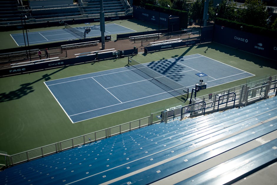 A sunlit empty tennis court with clear blue skies and shadows, ideal for sports stock images.