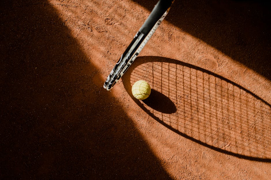 Tennis ball with racket shadow on a sunlit clay court.