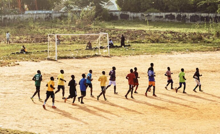 A group of young men practicing soccer on a dirt field under the sun.