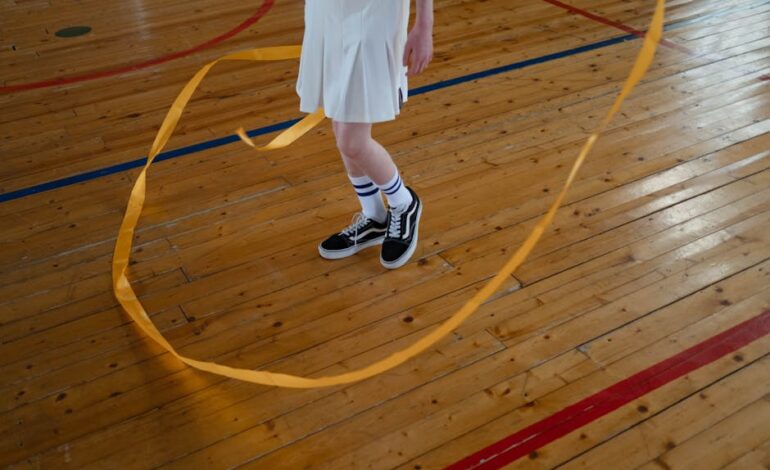 Young gymnast performing rhythmic gymnastics with ribbon indoors on wooden floor.
