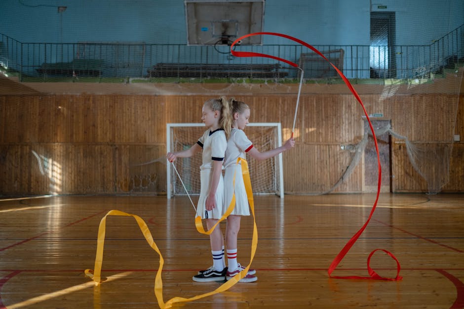 Two young gymnasts performing a ribbon routine indoors, showcasing their skills in rhythmic gymnastics.