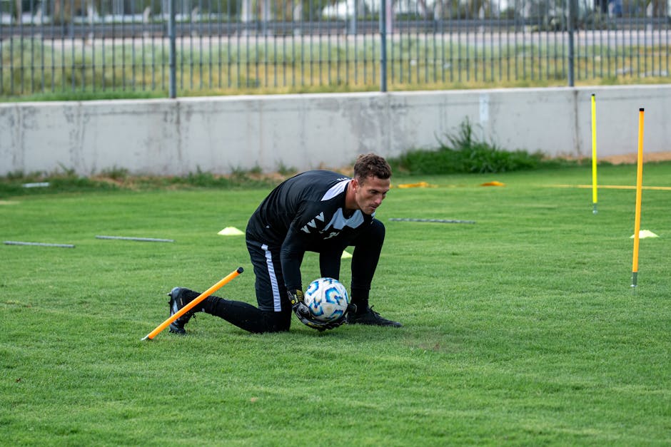 Athlete training on a grassy soccer field with a ball and training equipment.