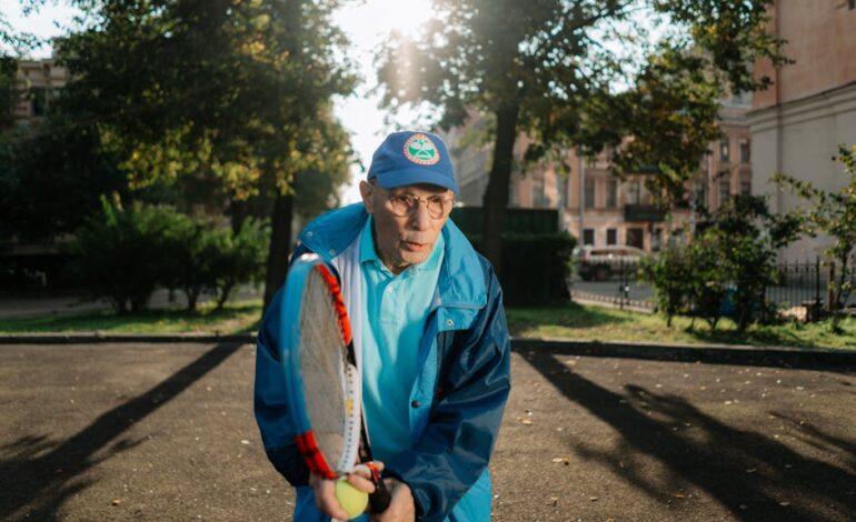 A senior man playing tennis outside, enjoying leisure activities in the park during the day.