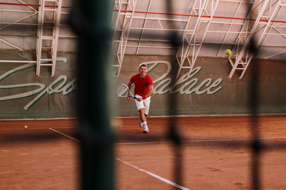 A male tennis player in action on a clay court at Sports Palace indoor facility.