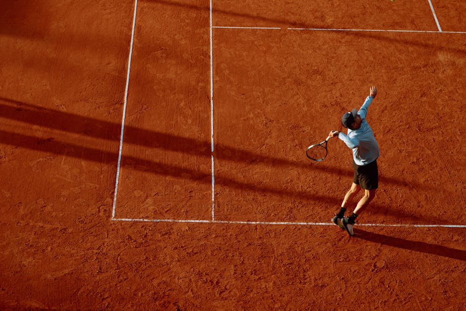 A dynamic shot of a tennis player serving on a clay court during sunset.