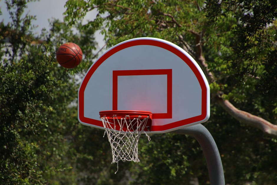 Basketball hoop with ball in mid-air on a sunny outdoor court.