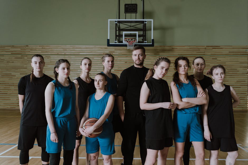 A women's basketball team posing with their coach inside a gymnasium.