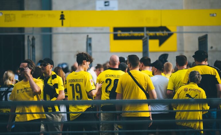 A vibrant crowd of football fans in yellow jerseys gathered at a stadium entrance during the day.