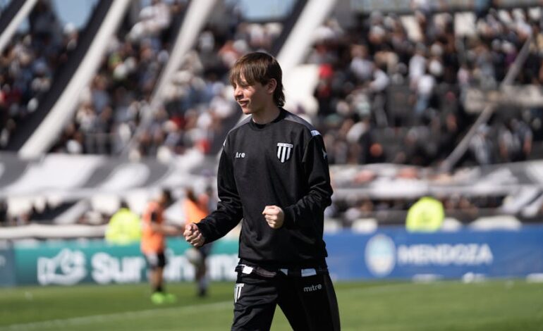 A young football player happily celebrates during a game, with a packed stadium in the background.