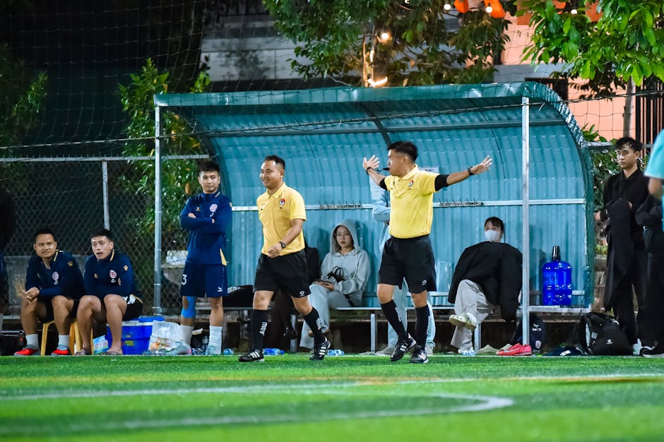 Football coaches and team watch intensely from the sideline in Hanoi night match.