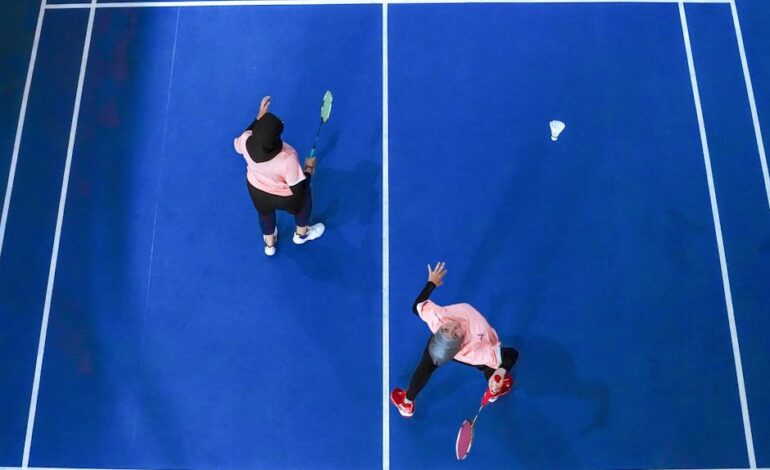 Top view of two women playing badminton on a blue court in Jakarta, Indonesia.