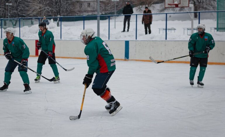Amateur ice hockey match in snow-filled setting with players in green uniforms.