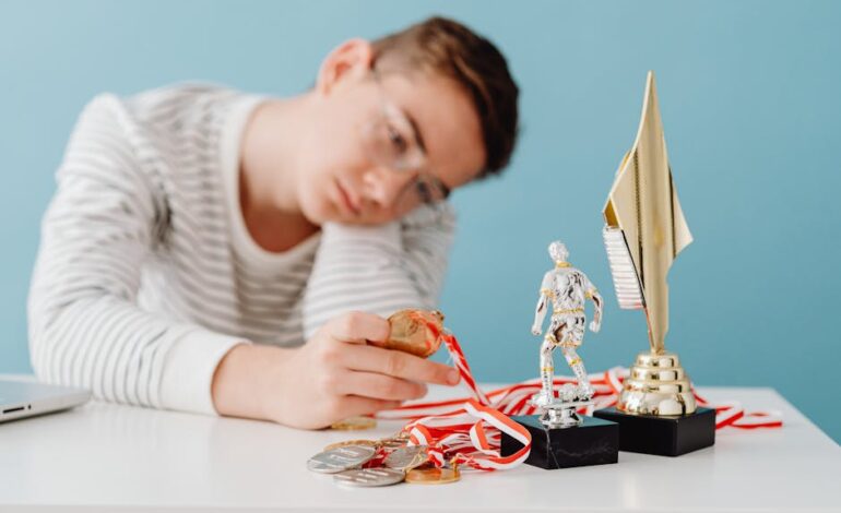 A thoughtful teenager sits by a table with various trophies and medals.