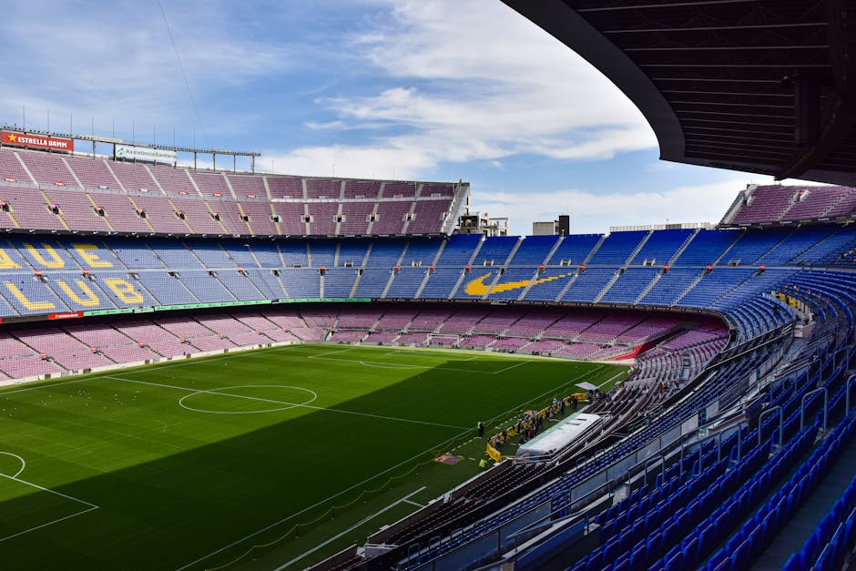 Wide view of the iconic Camp Nou stadium in Barcelona, showcasing its vast empty stands and lush green field.