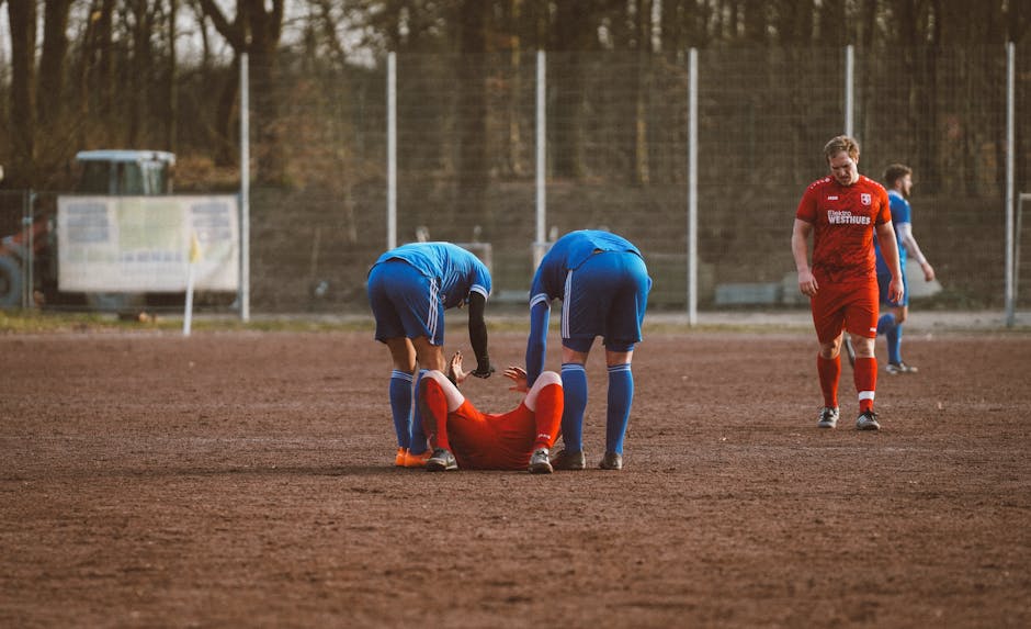 Players on a soccer field assist an injured teammate, highlighting teamwork and sportsmanship.