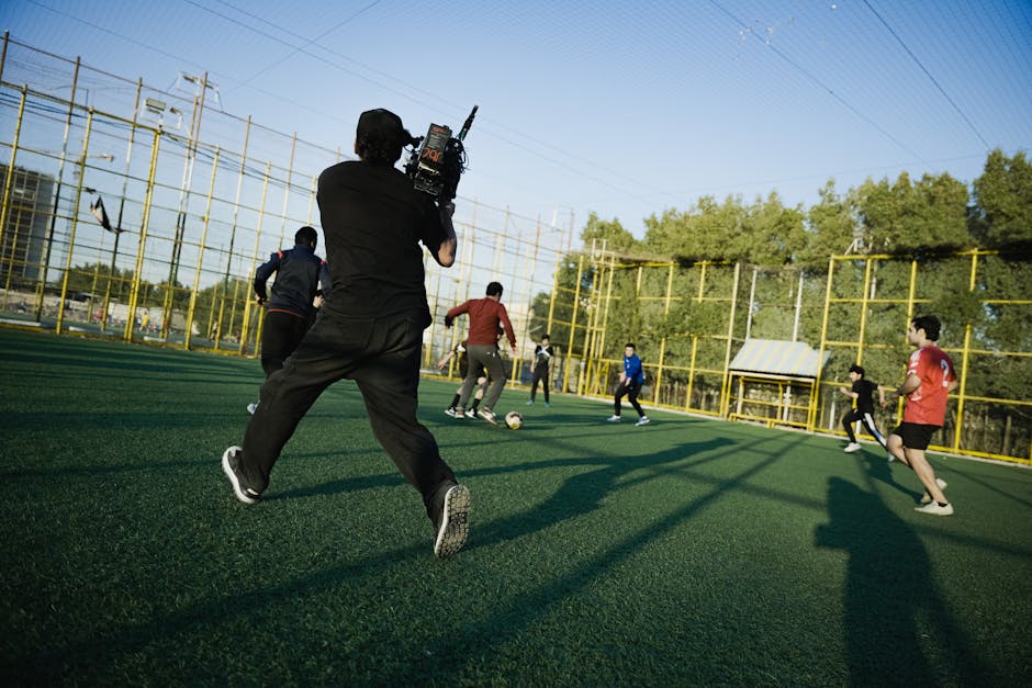 Cameraman captures an outdoor soccer game with players in action on a sunny day.