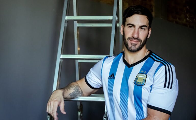Portrait of a man in an Argentina football jersey standing beside a ladder indoors.