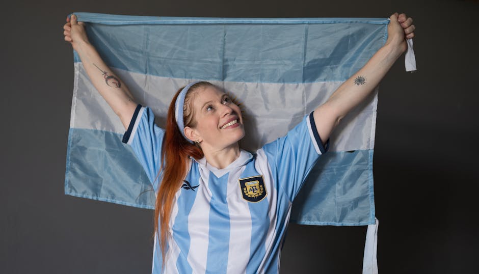 Joyful woman holding Argentina flag wearing national jersey indoors.