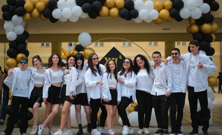 A group of teenagers posing under a balloon arch outdoors at a school celebration.