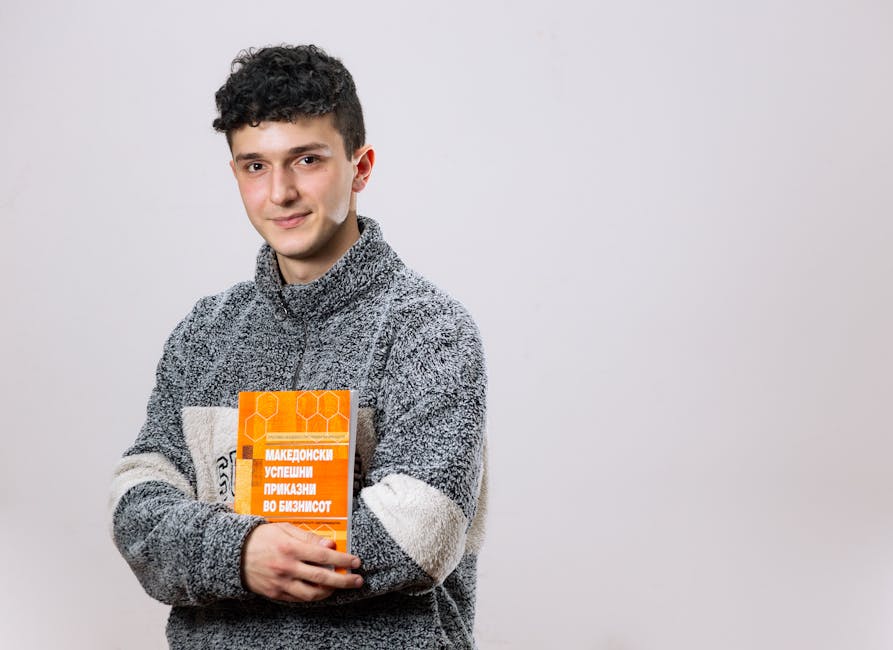 A young man smiles while holding a book in a studio setting, conveying a casual and educational vibe.