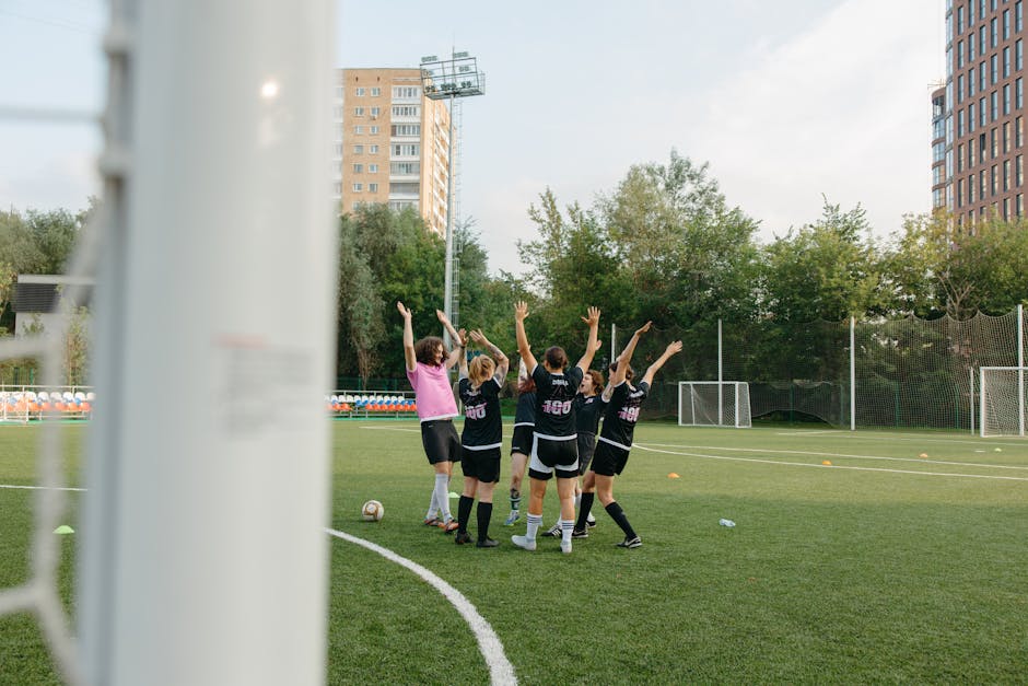 A women's soccer team in black uniforms celebrates a victory on an outdoor soccer field.