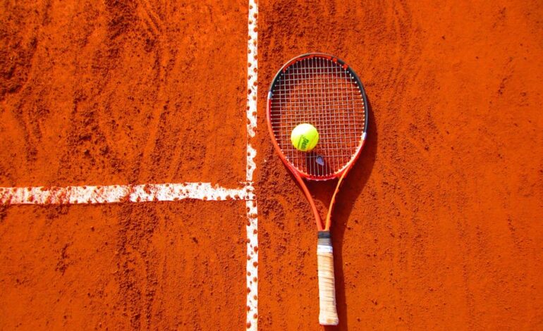 Tennis racket and ball on red clay court, ideal for sports-themed content.