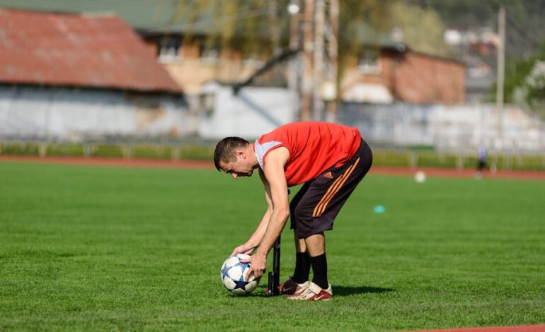 An athlete in sportswear preparing a soccer ball on a grass field during daytime training.