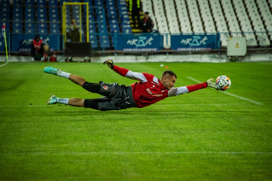 A soccer goalkeeper dives to make an impressive save during a match. Captured under stadium lights.