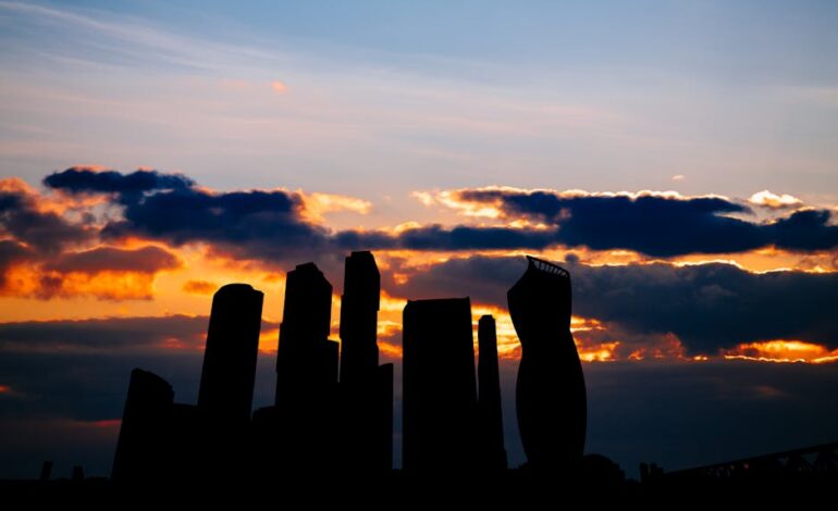 Silhouette of modern city skyscrapers against a colorful sunset sky with dramatic clouds.