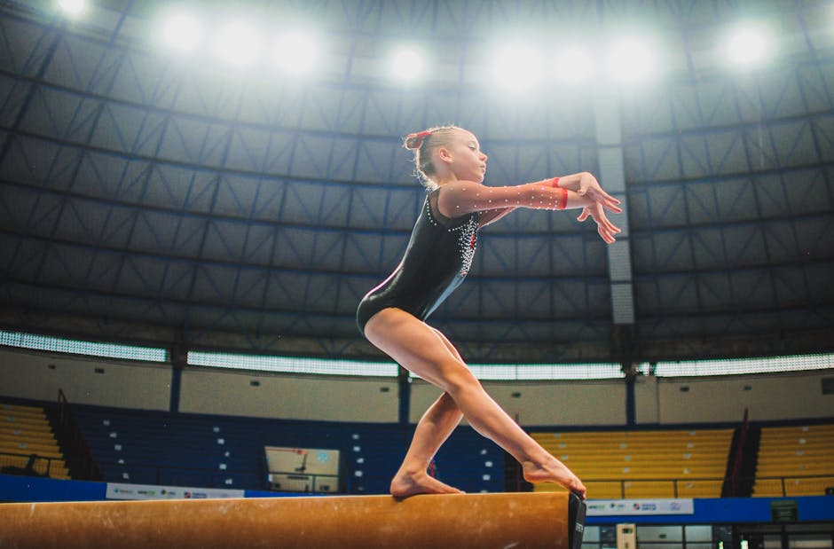 A young gymnast performing a routine on the balance beam indoors during a competition.