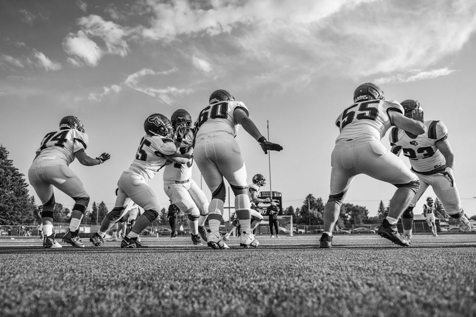 Black and white photo capturing a high school football game with players in motion on the field.