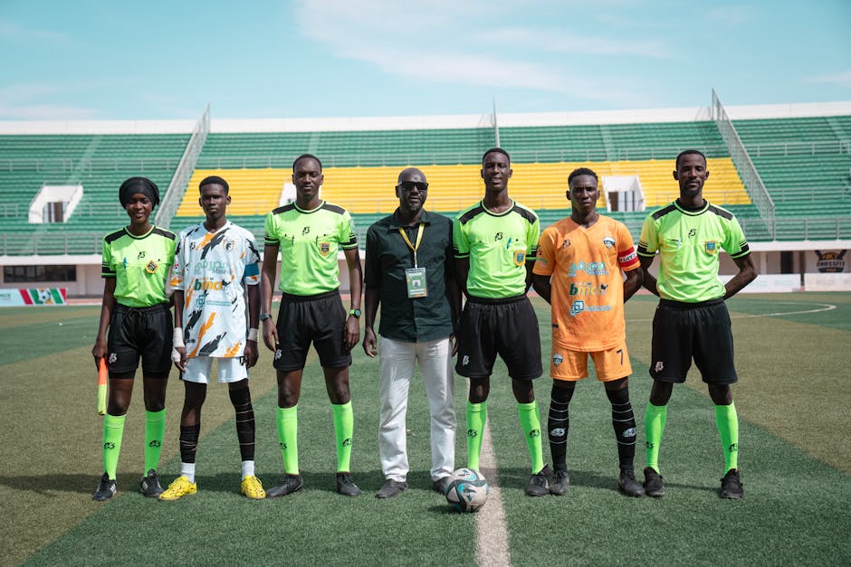 A soccer team with officials posing on a field during daytime at a stadium.