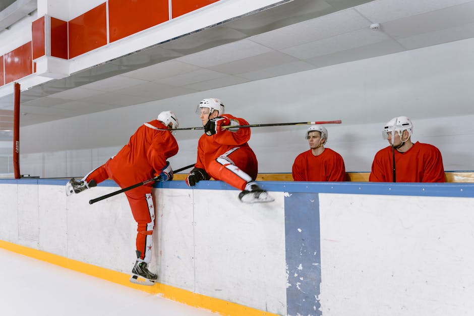 Hockey players practicing indoors wearing red uniforms and white helmets on an ice rink.