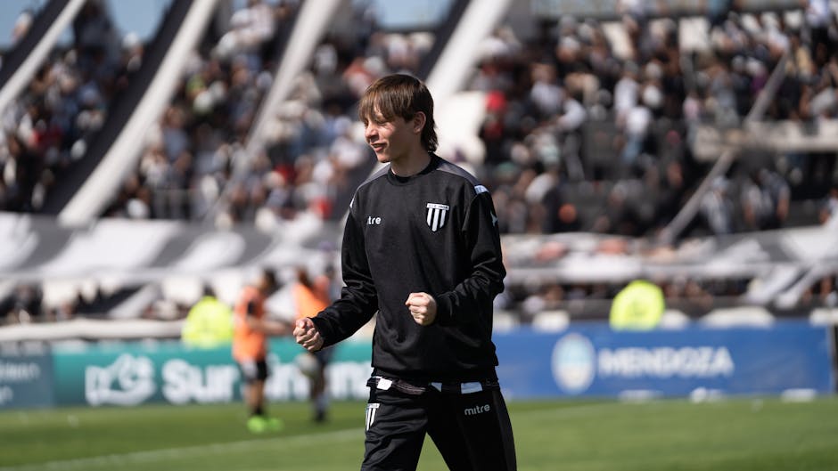 A young football player happily celebrates during a game, with a packed stadium in the background.