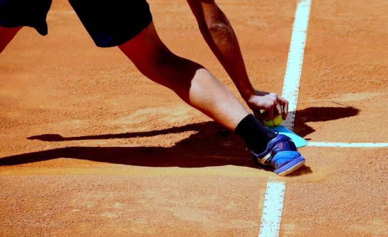 A tennis player reaching for a ball on a sunny clay court in Goiânia, Brazil.