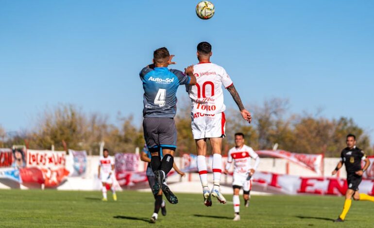 Soccer players in uniforms jumping to head the ball during an outdoor match on a sunny day.