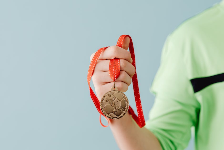 Close-up of a teenager holding a soccer medal on a red ribbon against a blue background.