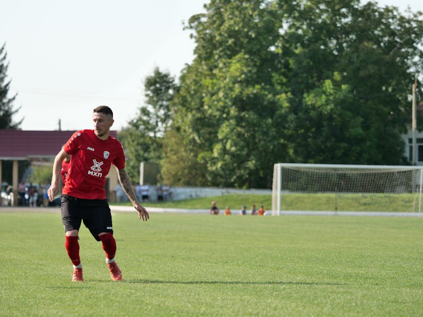 A soccer player in a red uniform on a sunny day, ready to make a move on the field.