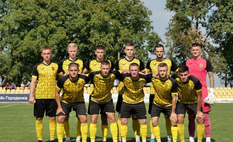 A young men's soccer team in yellow and black uniforms posing on the field before a match.