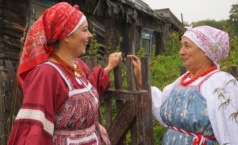 Two women in colorful traditional attire conversing outside a rustic house.