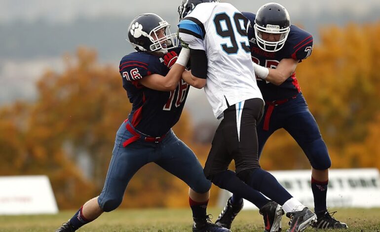 Football players in action during a competitive game on a field with autumn foliage.