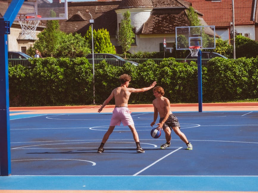 Two young men playing basketball on an outdoor court on a sunny day.