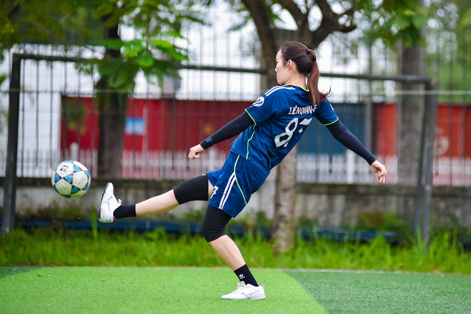 Young female soccer player kicking a ball on a lush green field in Hanoi, Vietnam.