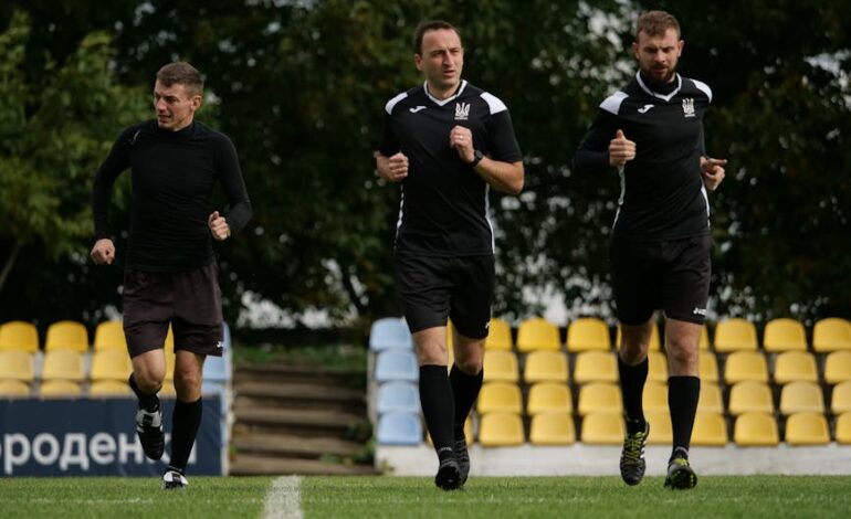 Three male referees running during a training session on a soccer field outdoors.