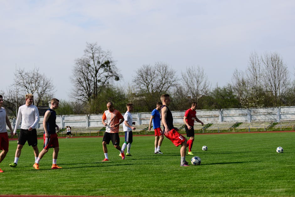 Athletes practicing soccer outdoors on a lush green field under clear skies.