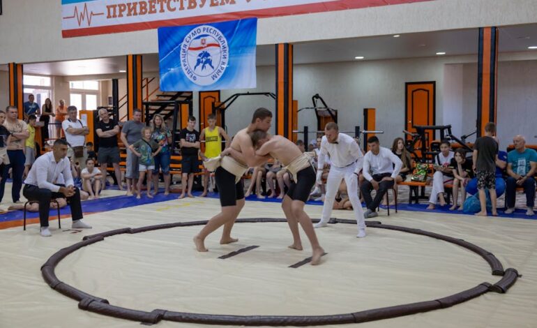 Young athletes engaged in sumo wrestling in a gym with spectators and a referee observing.