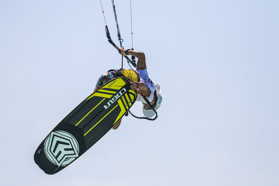 A kiteboarder performs an impressive trick against a clear blue sky.