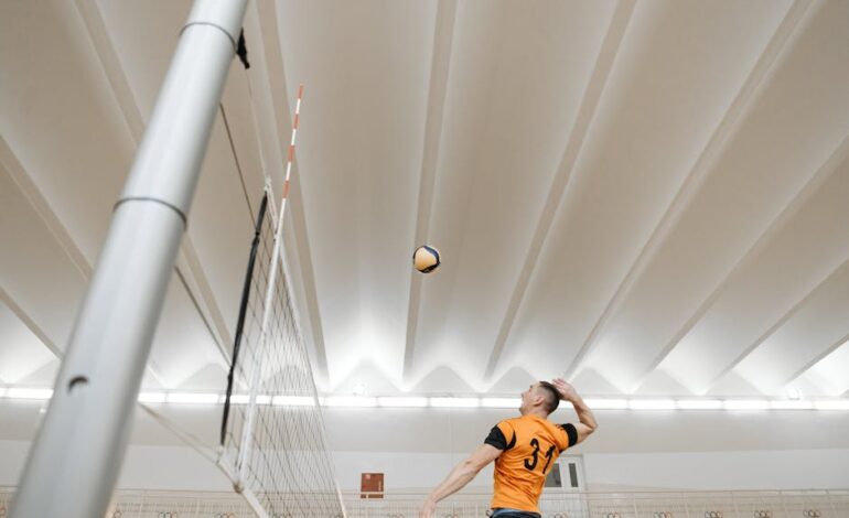 Male volleyball player jumps to spike the ball during an intense indoor game.